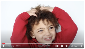 A screenshot of a Honey Baby youtube ad showing a child with curly hair, wearing a red sweater.