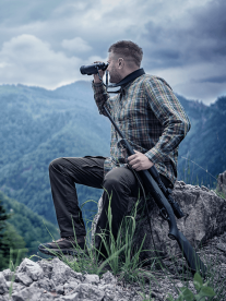 An outdoor man in the mountains looking through his Pulsar binoculars from Karoo out