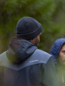 A man wearing a K-Way jacket and a beanie on a hike in the forrest.