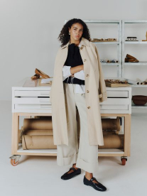 A woman wearing cream Poetry workwear and a trench coat looking serious at the office.