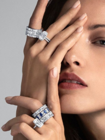 A beautiful brunette woman dripping in diamond rings holding her hand up to her face to show off the rings.