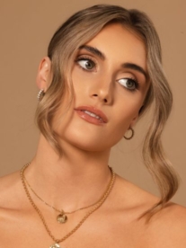 A stunning blonde woman modelling for Kelly Jay Jewellery wearing gold earrings and necklaces.