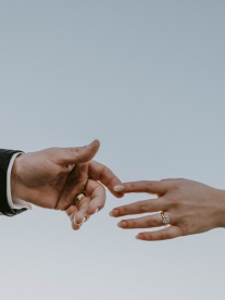 A man and woman's hands touching in front of a beautiful sky