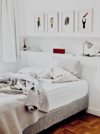 A white linen bed with comfortable blankets in a white room with artwork of birds above the bed