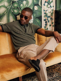 A well dressed young black man wearing a khaki polo shirt and chinos sitting on a mustard coloured couch