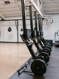 A gym with big gym equipment and boxing bags with wooden floors and white walls