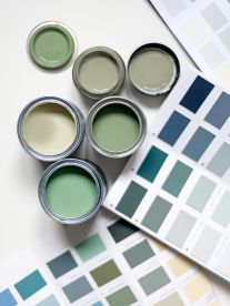 An image of six tins of paint in mint, sage, cream and olive green sitting next to paint swatch cards on the floor