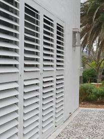 An outside view of a white house with a palm tree and white shutters. The floors are grey and white Moroccan tile.