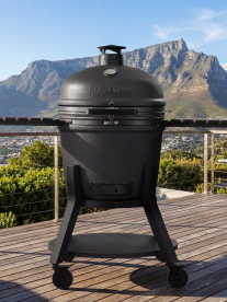Black outdoor ceramic grill on a wooden deck with mountains in the background.