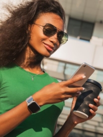 A pretty black woman with a takeaway coffee in her hand and her iphone in the other hand.