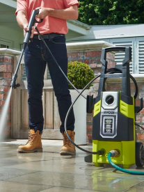 A man steam cleaning a patio with a Ryobi pressure cleaner.