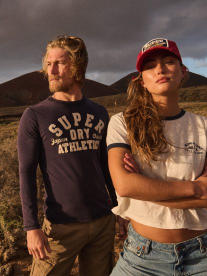Two people wearing Superdry clothing in a field with a mountain in the background.