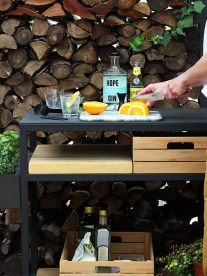 A man at a contemporary black and wood outdoor braai area preparing drinks