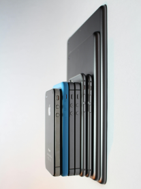 A stack of the latest iPhones and iPads in grey and blue tones.