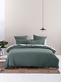 A styled, comfortable bed with green Linen House linen on.