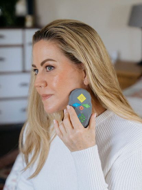 Woman holding a handheld skincare device against her cheek in a home setting.
