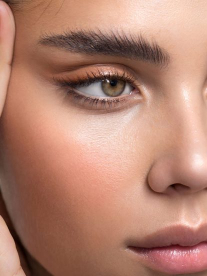 A beautiful young woman with olive skin and freckles who has had eyelash extensions and an eyebrow lamination