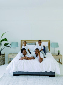 Family of 4 on white bed with white wall in background