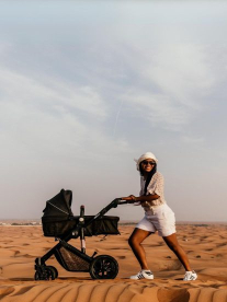 A lady in the desert pushing her baby in a designer Noola Baby pram.