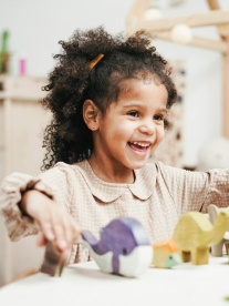 A cute little girl with an afro playing with her wooden toys at a table.