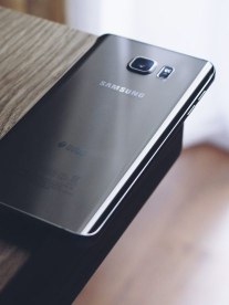 A slick grey Samsung phone sitting on a wooden table