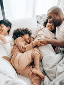 A mixed race family with children lying on a comfortable bed and having fun and laughing