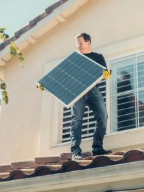 A man standing on his roof, putting in solar panels at his home.