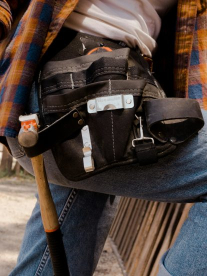 A construction worker wearing a plaid shirt and jeans with a waist tool belt