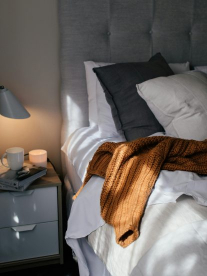 A beautifully made bed with a grey headboard and lots of throws.