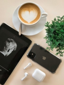 An iPhone on a coffee table sitting next to a cappuccino.