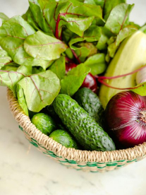 An African basket with a thin green woven border, filled with fresh vegetables like cucumber, red onion, lettuce and banana.
