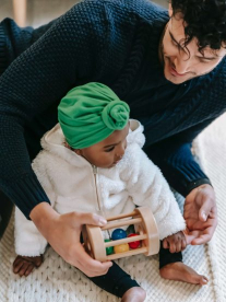 A dad and his baby playing with a toy and wearing a baby turban